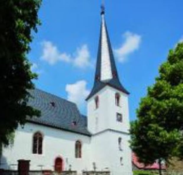 Zu sehen ist die weiße Kirche Essenheim. Auffällig ist der spitz zulaufende Kirchturm.