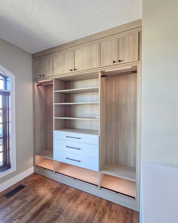 Walk-in closet with long hang sections, upper cabinets, open shelving, drawers, and slanted shoe shelves. Lighting and black hardware complete this system.