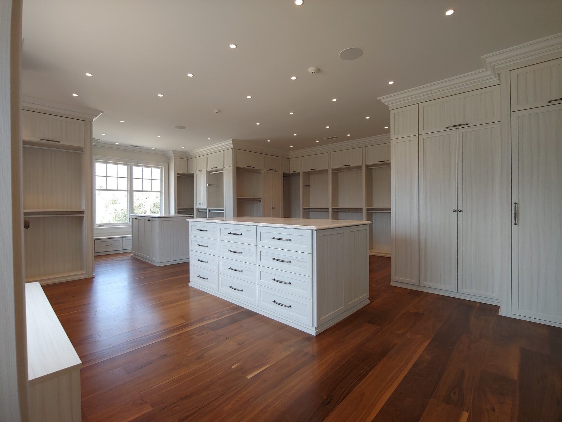 Large closet in textured white material with double center islands and windows