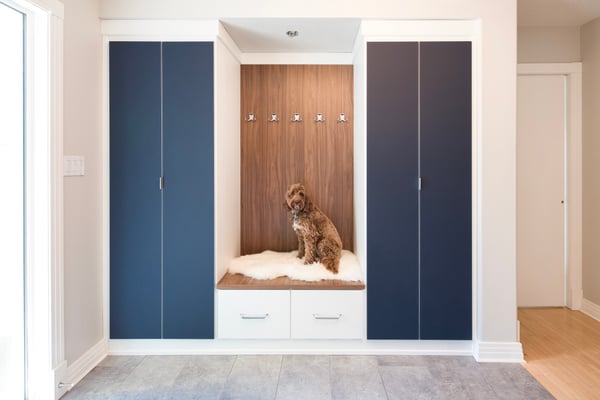 A mudroom with dark blue and warm wood tones. Floor to ceiling storage for coats and shoes with a bench in the middle. Hooks provide and easy way to hang every day items.