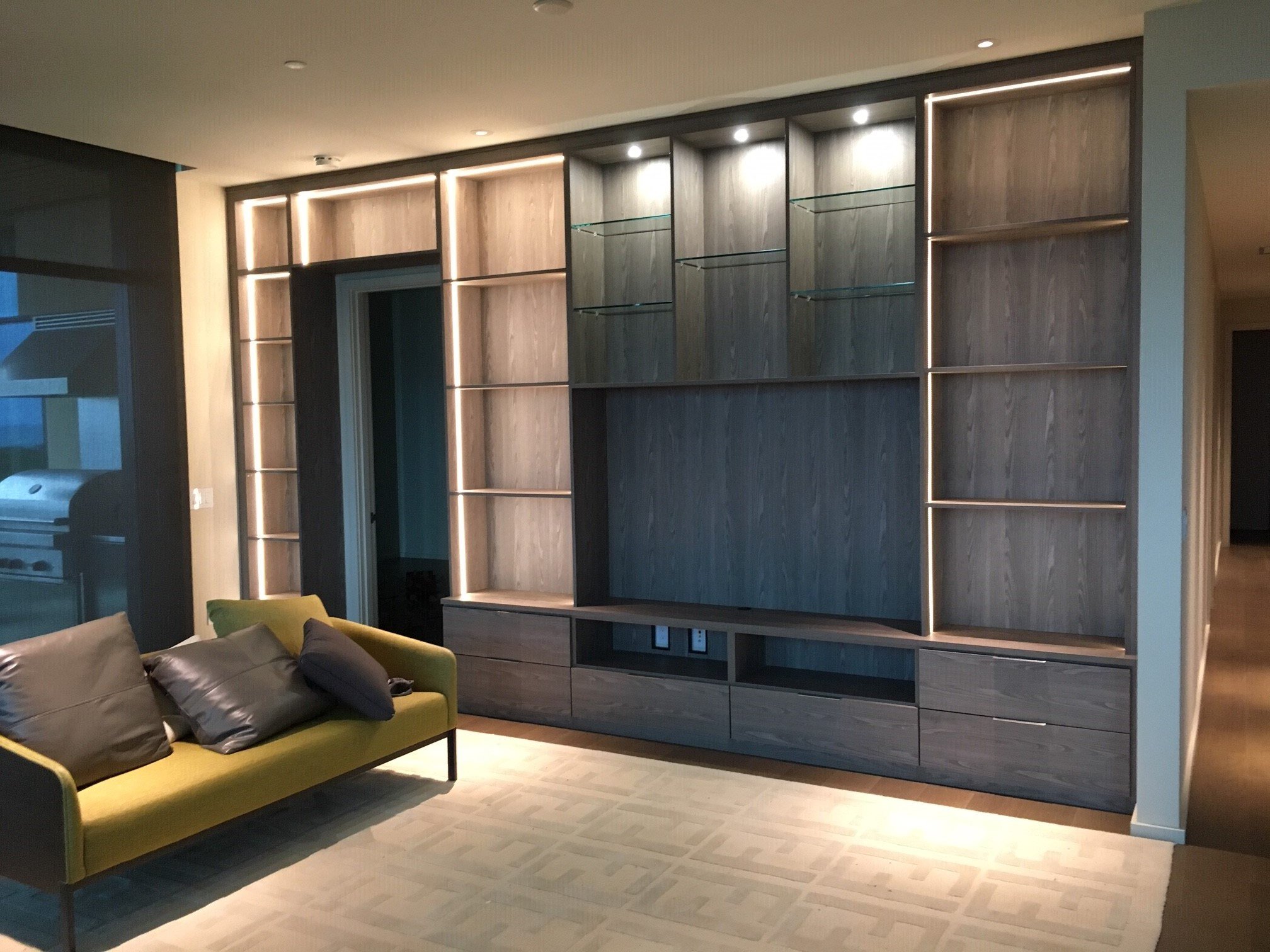 Entertainment and storage center with puck lighting and glass shelving by California Closets Hawaii.