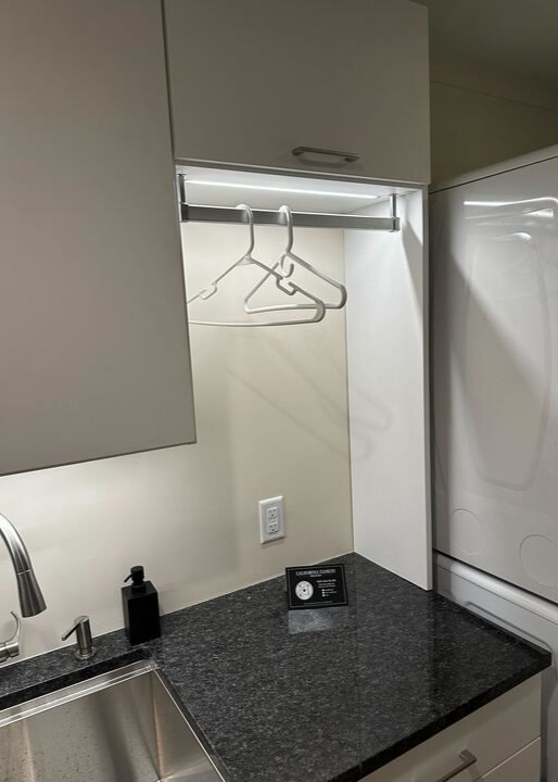 Wilmington - Custom closets - Laundry room storage with LED-lit hanging rod and black granite countertop.