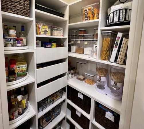 White pantry with a variety of open shelving and drawers stores dry goods, recipe books and more.