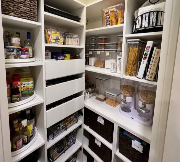 White pantry with a variety of open shelving and drawers stores dry goods, recipe books and more.