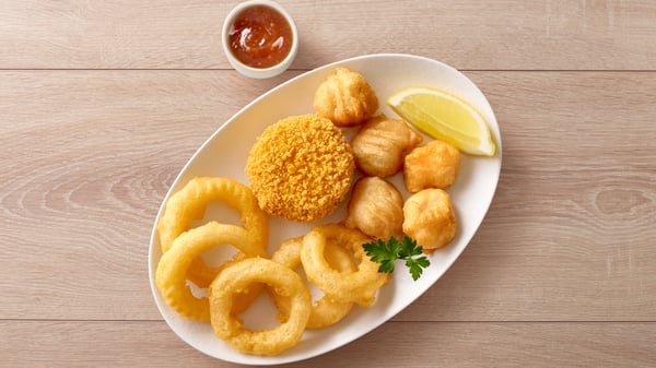 A fish cake, hake nuggets and onion rings on a white plate.