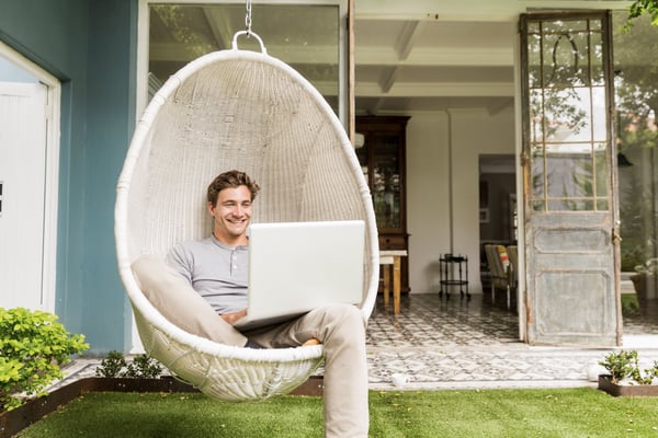 Man typing on laptop sitting in hanging chair outside