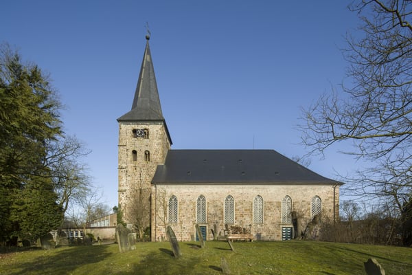 Ein Kirchengebäude mit einem Friedhof, umrahmt von Bäumen.