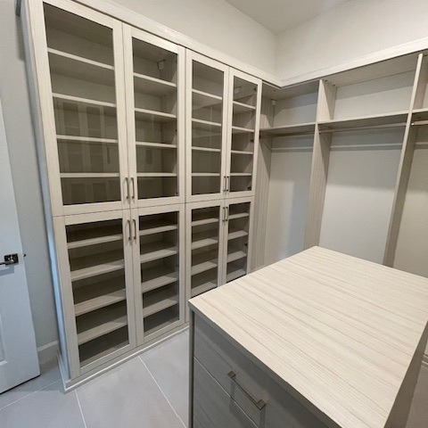 Custom master closet with Tuscan Moon finish, Bellissima White backing, matte nickel hardware, glass door inserts, and wardrobe pull-downs.