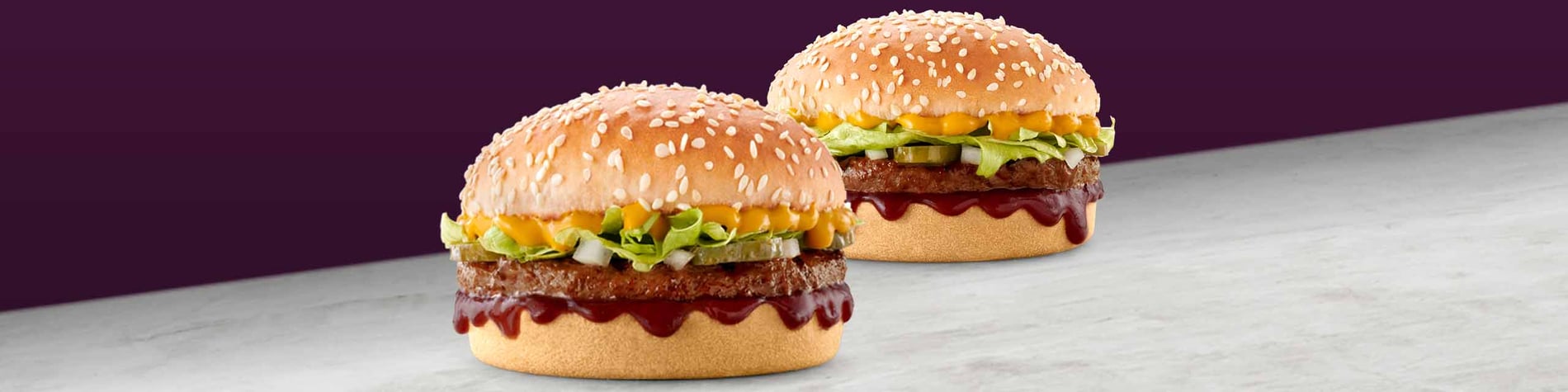 Two burgers on a grey surface against a purple background