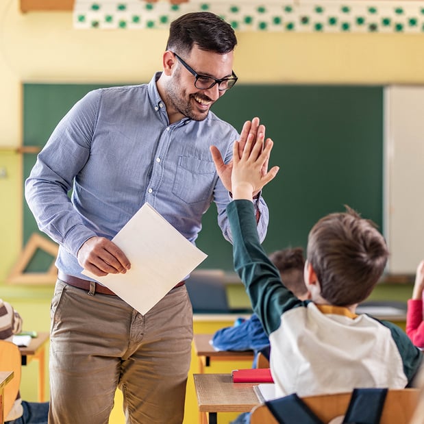 A male teacher high-fiving a young boy in a classroom