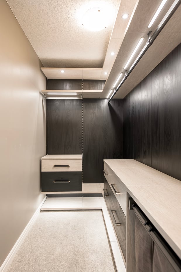 Narrow walk in closet, design in a modern style with floating shelves, contrasting colors, black backing, and lighting.