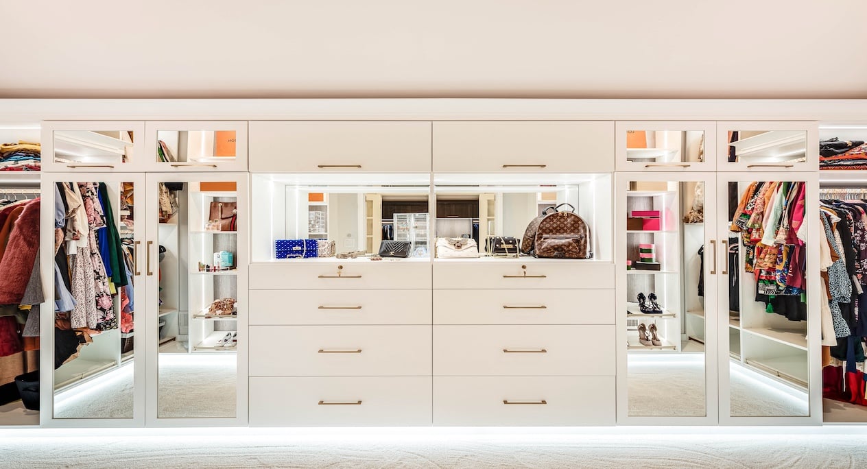 Her walk-in closet with lighting and white drawers and mirrored cabinets.