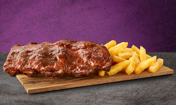 A single rack of beef ribs with a side of chips on a wooden board placed on a grey surface with a grey background.