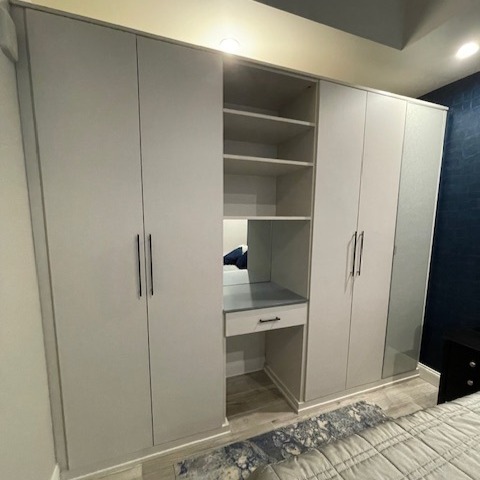 Custom guest room storage in Linen finish with black Regatta handles, matte aluminum finger pulls, elite round vanity pulls, aluminum frame door with woven frost glass, and silver matte countertop.