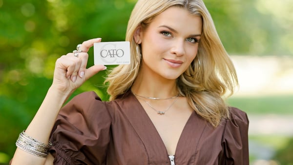 Woman is smiling and holding up a Cato Fashions gift card.