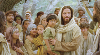 Christ with a large group pf peole behind Him, holding a child in His arms.