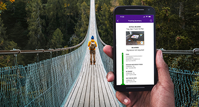 A image of FedEx mobile app on phone with a person walking on a bridge in the background