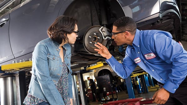 Two Pep Boys Mechanics work on the rim of a car that is up on a platform