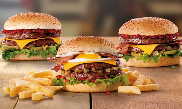 Three beef burgers in between two servings of chips on a wooden table.