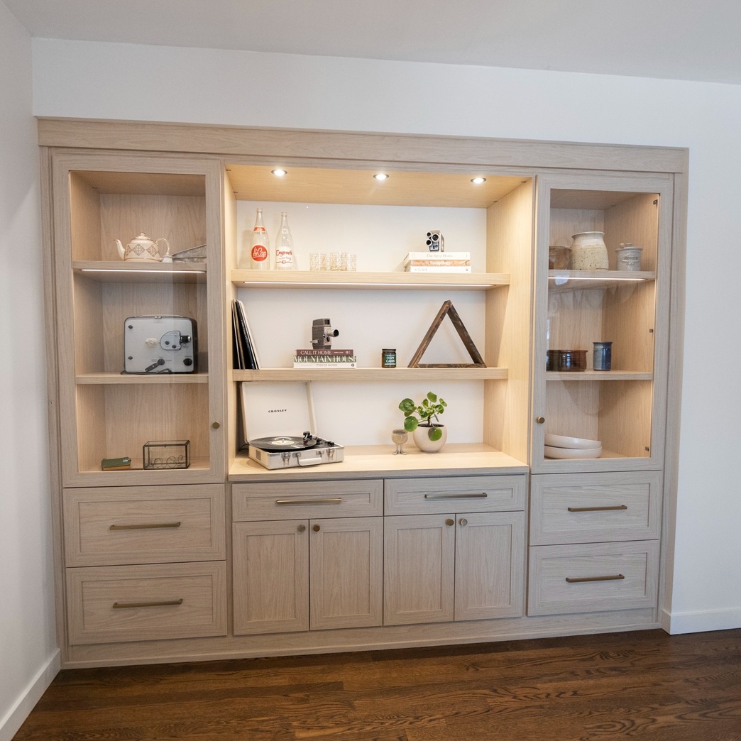 Dining room storage in a natural wood finish with open shelving and lighting and closed storage.