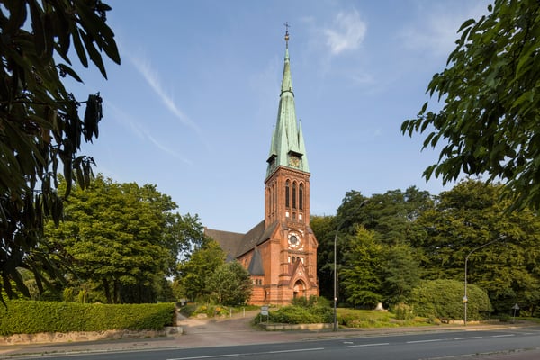 Kirche aus Backstein mit einem spitzen Kirchturm, umgeben von Rasen und Bäumen.