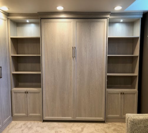 Custom Murphy bed with desk, shelves, and cabinets in light wood by California Closets Northern Michigan