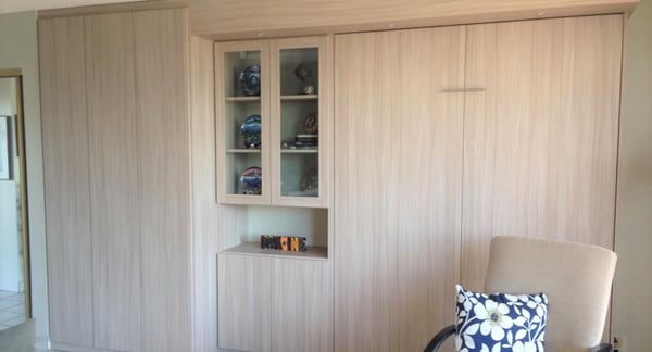 Wardrobe wall unit with pull-down bed in light finish.