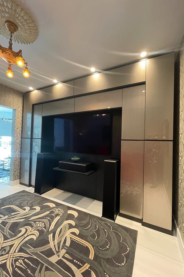 Modern custom entertainment wall with dark cabinetry, integrated lighting, built-in television, and concealed storage.