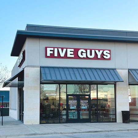Exterior photograph of the entrance to the Five Guys restaurant at 6451 East NW Highway in Dallas, Texas.