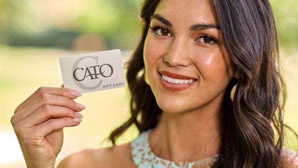 Woman is smiling and holding up a Cato Fashions gift card.