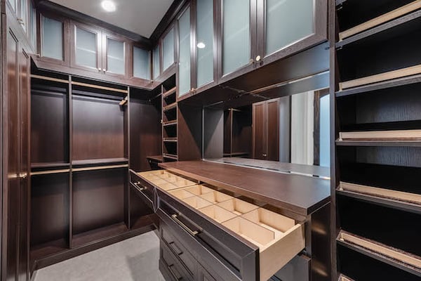 Custom, luxury walk-in for him with dark woodgrain, glass doors and belt storage.