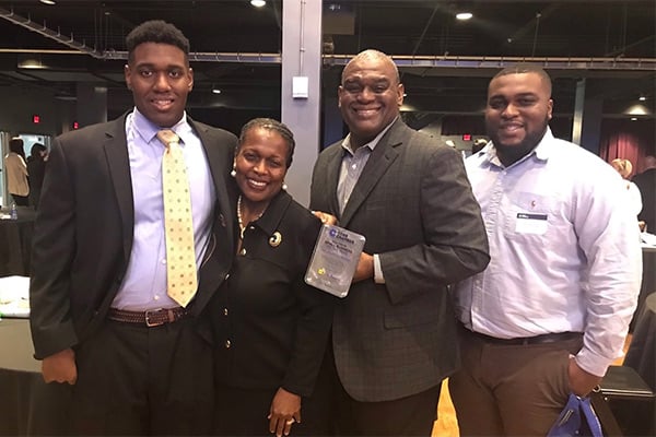 Joseph and family in business attire smiling while holding award from Cobb Chamber of Commerce