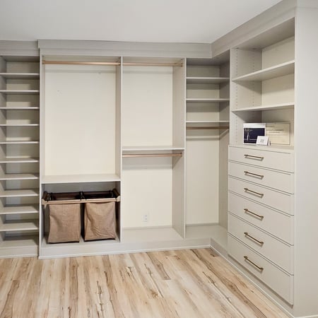Walk in closet designed in a taupe colour with gold hardware, hanging, pull out laundry baskets, and shoe shelves.