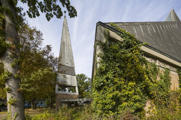 Das moderne Kirchengebäude mit freistehendem Glockenturm und Begrünung.