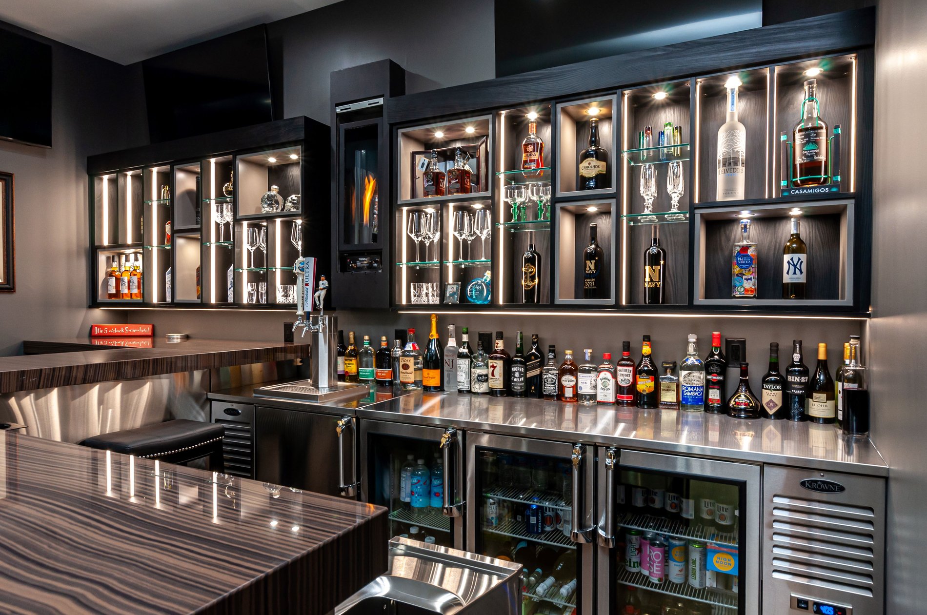 Home Bar in black with lighted cabinets filled with liquor bottles and glassware by California Closets Northern New Jersey.
