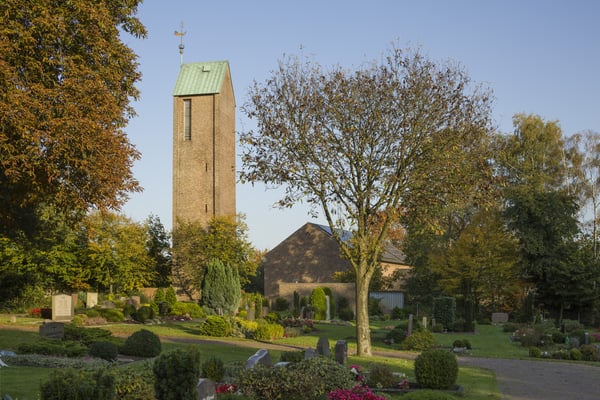 Kirchengebäude mit Friedhof und Bäumen.
