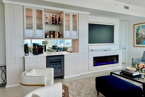 Custom fireplace and cocktail bar in Tuscan Moon and Dove with shaker doors featuring reeded glass inserts, City Light glass knobs in satin brass by Schaub, glass shelving, and mirrored backing for a sophisticated, functional space.