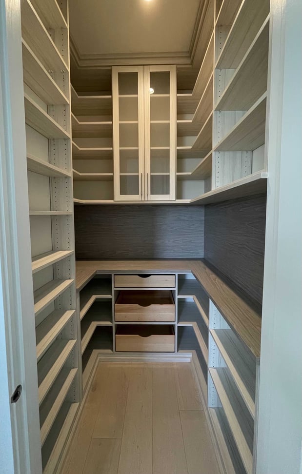 large pantry with floor to ceiling shelving and L-shaped counter in white and grey wood tones
