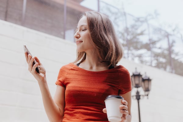 Woman looking at phone holding coffee