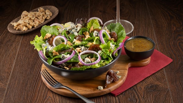 A salad with blue cheese, figs, walnuts, red onion, lettuce, fresh rocket and honey mustard salad dressing on the side with a glass of wine from the Turn ‘n Tender menu.