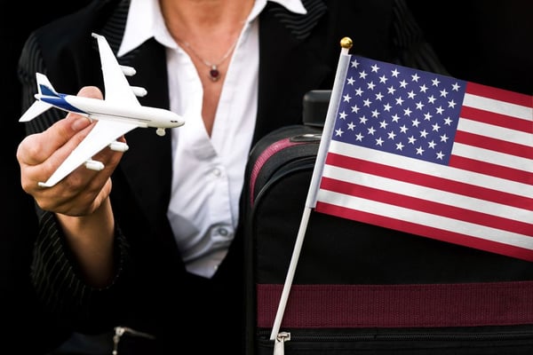 ビジネスウーマンが、おもちゃの飛行機の旅行バッグとアメリカ合衆国の国旗を持っている