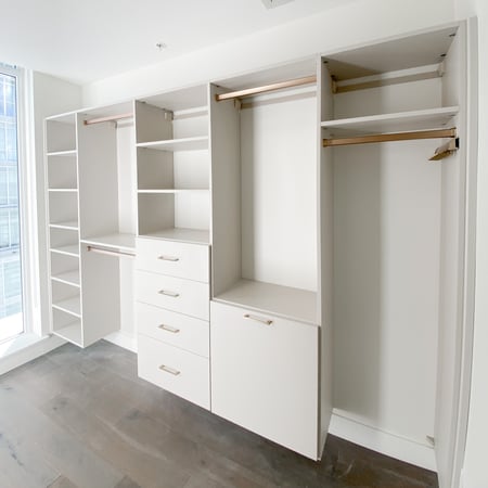 Walk in closet in a light matte finish with gold hardware, drawers, pull out laundry hamper, and open shelving.