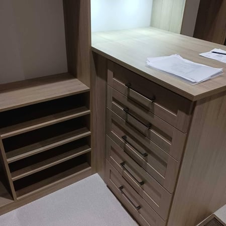 Wood finish shelves, drawers, and a countertop inside a closet.