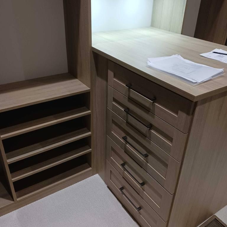 Wood finish shelves, drawers, and a countertop inside a closet.