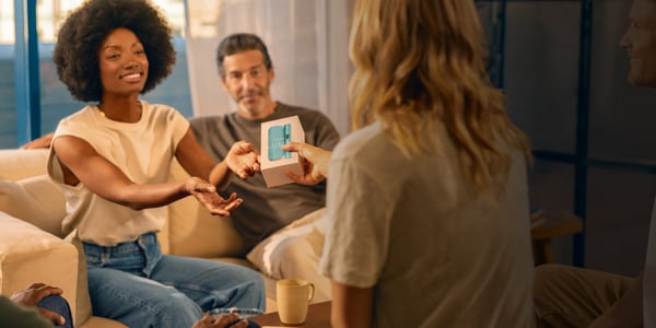 Femeie înmânează o cutie cu un iqos iluma unei alte femei.