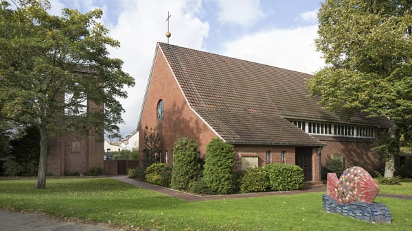 Das Kirchengebäude mit einer bunten Fischskulptur auf einer Rasenfläche.