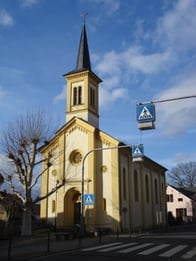 Zu sehen ist die weiß-gelbe Kirche Nieder-Olm vor blauem Himmel.