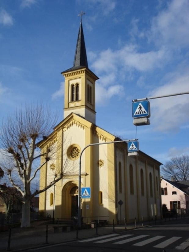 Zu sehen ist die weiß-gelbe Kirche Nieder-Olm vor blauem Himmel.