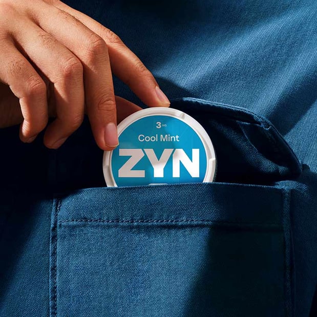 Dłoń chowająca opakowanie saszetek ZYN Cool Mint do kieszeni granatowej koszuli