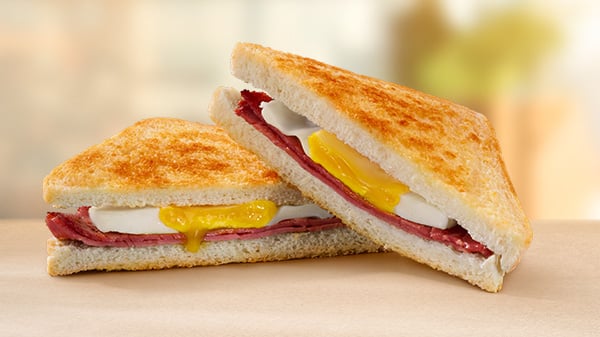 A Macon & Egg Toasted Sandwich on a brown surface with a blurred background.